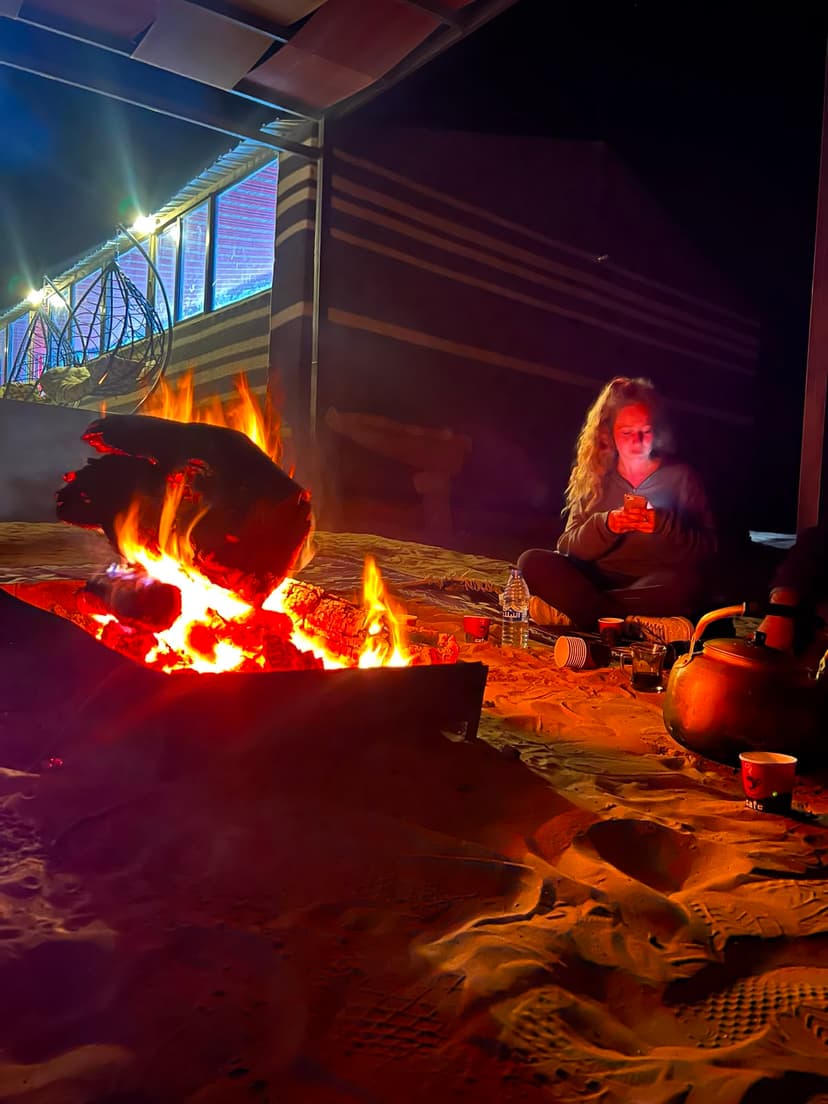 Guest sitting peacefully next to glowing Bedouin campfire with traditional kettle and night sky